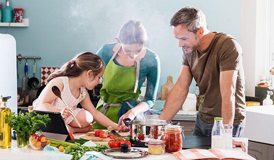 A family cooks in a kitchen, focused on a recipe with various ingredients laid out on a table