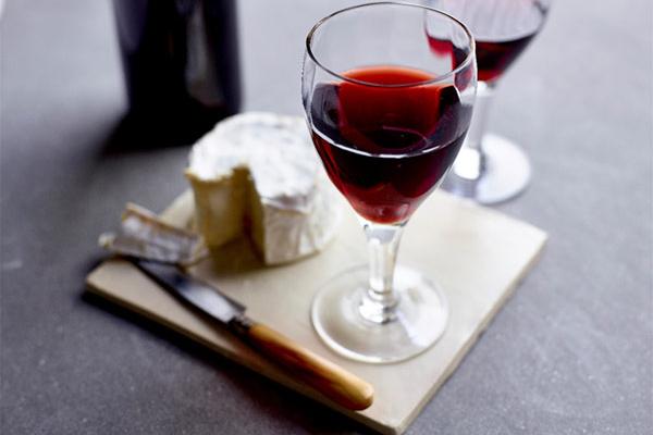 A glass of Bordeaux wine on a board with a round of Camembert